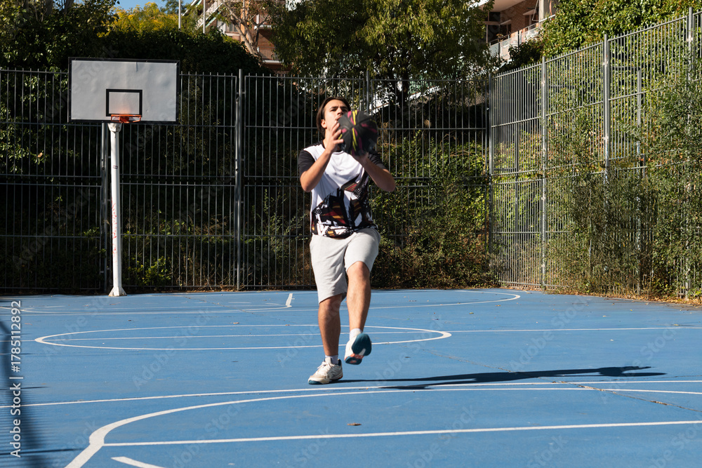 Obraz premium Young man playing basketball on an outdoor court