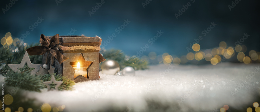 Obraz premium Christmas lantern with warm glow, fir branches, ornaments and lights on snow. Panoramic holiday card with blue background.