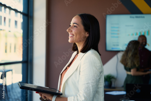 Side view of smiling young businesswoman in smart casual with tablet in boardroom at office