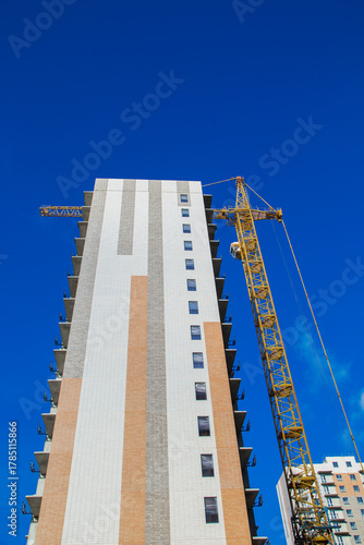 The high-rise structure, erected with a crane, combines different materials and textures against a bright blue sky, highlighting the activity of urban construction. High quality photo