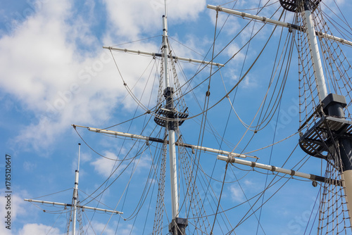 Masts of a sailing ship against a blue sky with clouds.