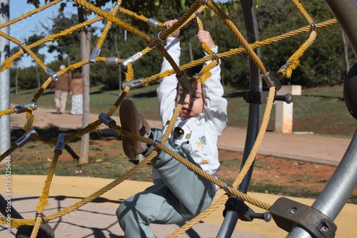 A white Caucasian boy in an outdoor play park, playing on a climbing frame