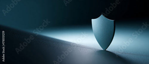 Minimalistic blue shield standing on textured surface with dramatic lighting symbolizing protection and security concept