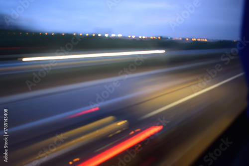 image of a blurred, motion-filled view of a highway or road, taken possibly from a moving vehicle. The scene includes streaks of red and white lights, which are characteristic of long-exposure