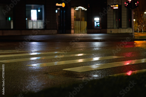 Wet Pedestrian Crosswalk at Night with Reflections of City Lights and Traffic Signals on Asphalt Street Surface