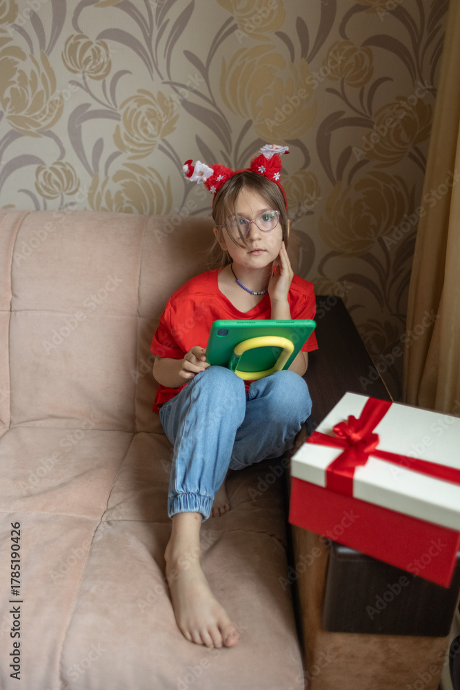 Fototapeta premium A girl in a Santa Claus hat opens a gift. It's Christmas time.