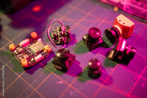 assortment of fpv drone components including cameras and circuit boards on a work surface, neutral background, clear negative space, clean composition, balanced framing, minimalist layout, editorial