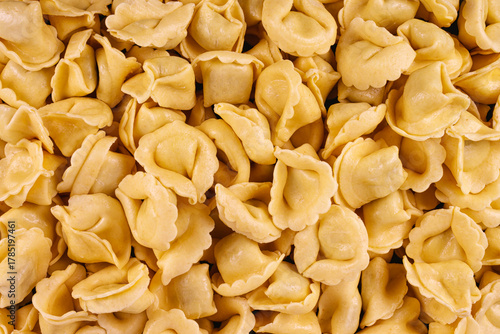 Close-up of raw yellow tortellini pasta in a full-frame composition. Fresh and uncooked, this Italian food background highlights texture and shape, ideal for culinary design and advertising.