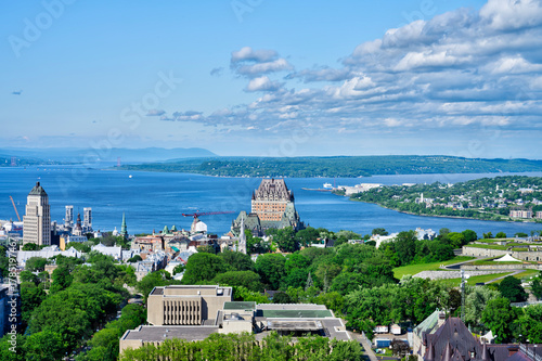 Panoramic summer view of Old Quebec with Château Frontenac, St. Lawrence River, and lush greenery under a blue sky. Iconic Canadian cityscape perfect for travel and editorial content.
