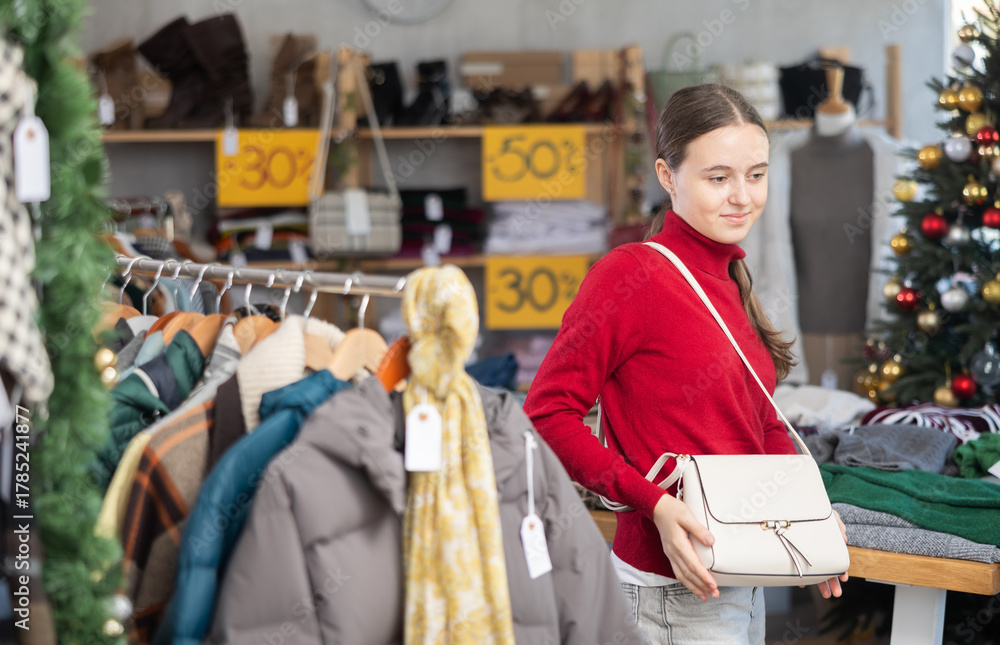 Obraz premium Teenage girl buyer choosing handbag in clothing store decorated for christmas