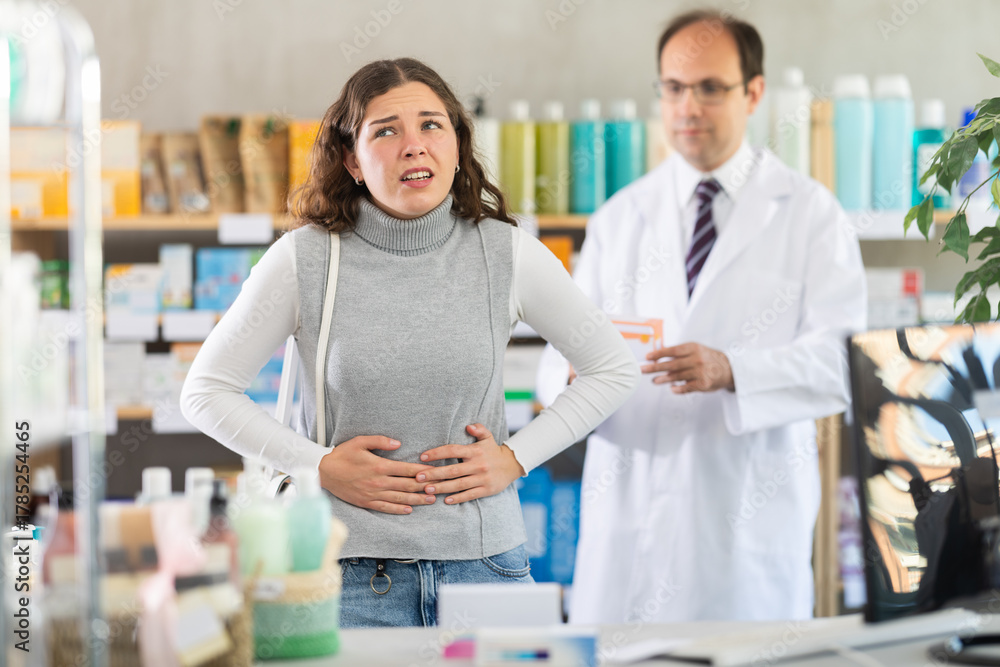 Obraz premium Young woman suffering from stomach pain. Male pharmacist offering stomach pain pills