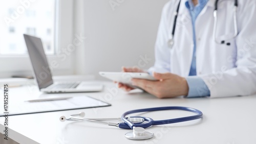 Closeup of blue stethoscope is lying on the table near female doctor reviewing prescription on digital tablet, representing digital healthcare workflow in contemporary medical setting. Medicine
