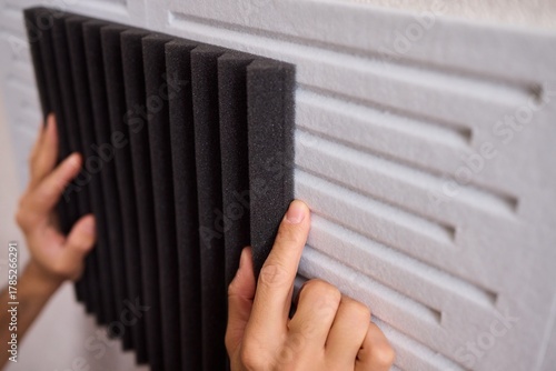 Closeup of foam insulation method, Hand pressing textured acoustic foam onto wall surface, Detailed shot of fingers securing black foam panels on gray wall Comparison of different foam rubber and