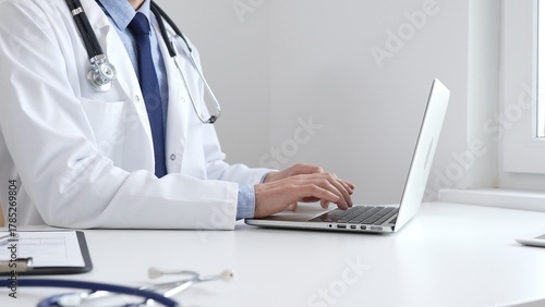 Male doctor is typing on laptop, updating electronic patient records with focused concentration, representing digital transformation in healthcare workplace. Medicine and healthcare