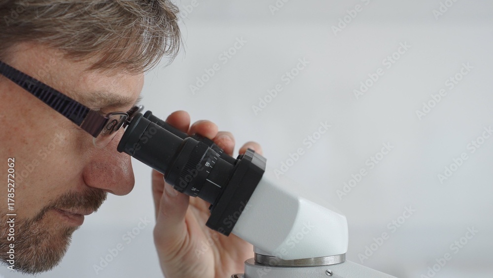 Obraz premium Close up of a male scientist looking through a microscope, conducting research and analysis in a laboratory setting, showcasing scientific investigation and discovery. Medicine and science concept