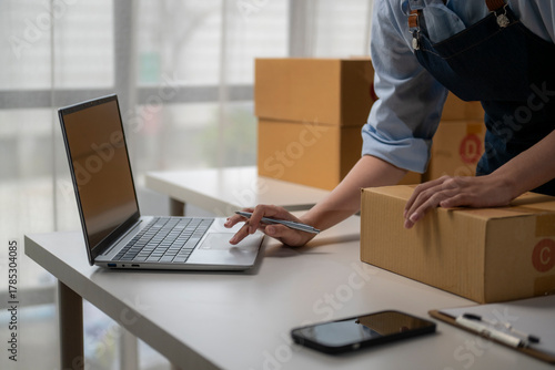 Online seller preparing cardboard box for delivery and using laptop