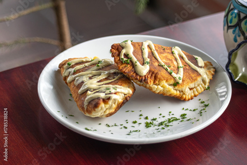 Close-up photograph from above of fried empanadas with sauce on a white spiced plate on a Corinthian table
