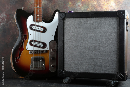 Vintage electric guitar with guitar amplifier against a brown concrete wall.