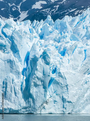 Majestic Perito Moreno Glacier with snow-capped mountains in Patagonia, Argentina. Vivid blue tones of the ice contrast with the dark slopes, highlighting the raw beauty of nature.