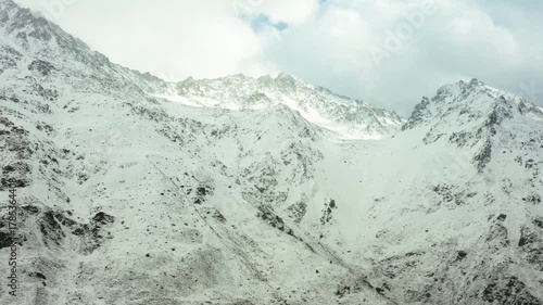 An aerial view of the majestic North Caucasus mountain range in Russia, blanketed in pristine snow. The footage captures the rugged, dramatic peaks and valleys under a vast, cloudy sky, showcasing the