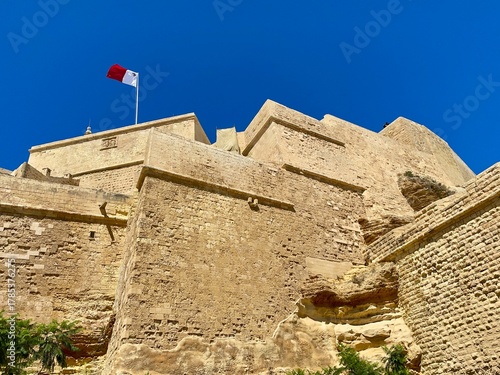 Historic Fortifications with Maltese Flag Under Clear Blue Sky