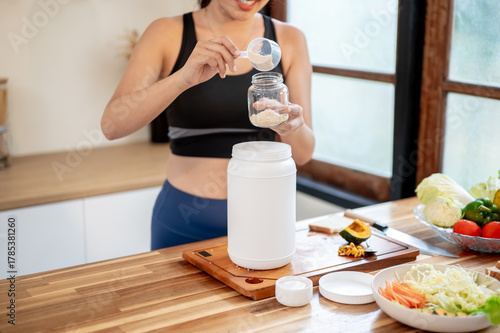 Woman using spoon scooping powder making protein shake drink in glass jar at kitchen cooking counter