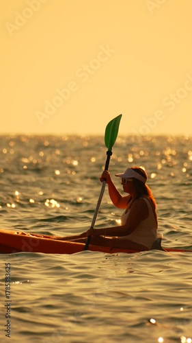 Kayaking sunset woman paddles orange kayak across sparkling ocean water enjoying a golden light vacation Vertical video