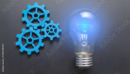 Light bulb shining over blue gear mechanism representing innovation, teamwork, and inspiration.