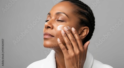A photograph of an African American woman applying facial cream to her face