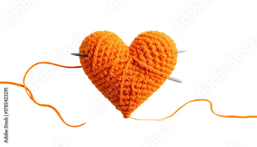Knitted orange yarn heart impaled by needles against dark