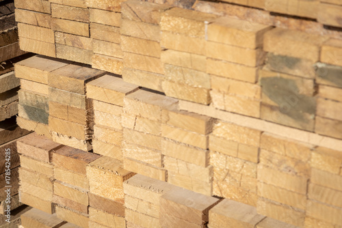 Stacked wooden planks in a lumberyard, showing various shades and textures of the wood, arranged in neat rows.