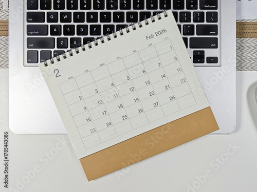 Minimalist desk setup with a 2026 February calendar placed on a laptop keyboard, concept of planning, scheduling, and time management for the new year.