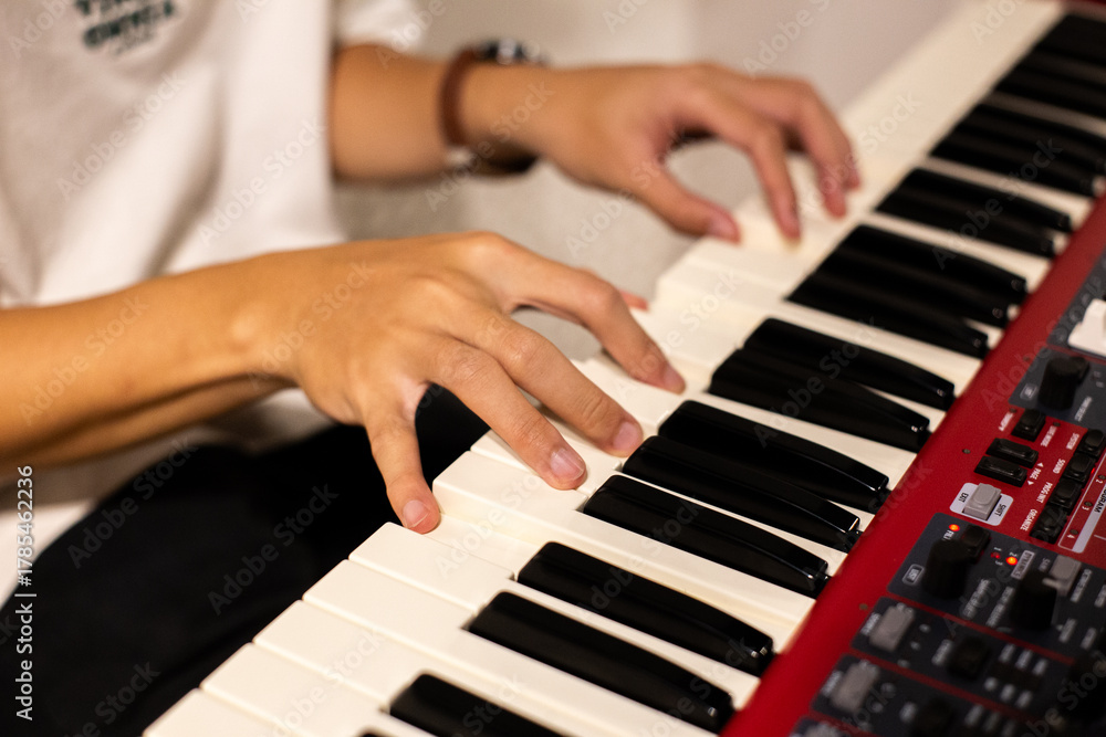 Obraz premium Close-up of a musician playing a red electronic keyboard indoors, showing focused hand movements across the piano keys.