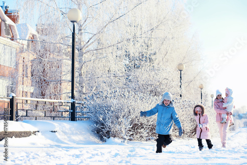 Family with children play snowy winter games in the park. Winter holidays and family vacation. Winter walk on the street on a sunny frosty day.