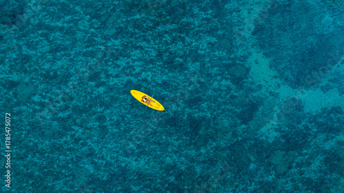 Aerial view woman bright yellow kayak with in the vast expanse of crystal clear turquoise water. The seabeds rocky texture is visible beneath the surface, concept marine environment	
