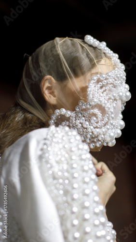 Fashion model in pearl-covered veil and dress, artistic couture design with delicate light and surreal atmosphere