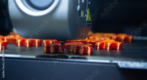3D printer close up. Working 3D printer in process of printing object from molten orange plastic. 3D printer creating model by flowing liquid plastic from extruder of printer. 3D printing technology