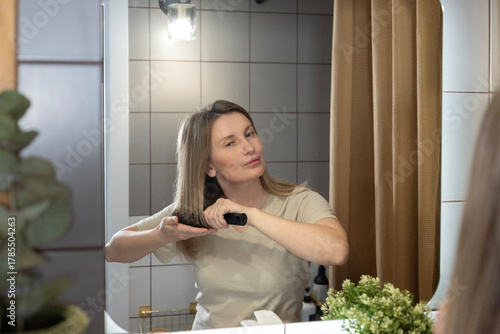 Mirror reflection, a young woman combing her hair in front of a mirror in the bathroom. Morning care, personal hygiene, and the beginning of a new day