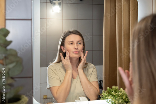A daily beauty ritual. A woman applies moisturizer to her face in the bathroom, taking care of her skin and maintaining its youthfulness. Morning care, a healthy lifestyle, and self-improvement in det