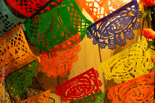 A colorful array of paper lanterns hang from the ceiling. The lanterns are of different colors. Mexican Day of the Dead tradition, offerings, food, colors, decorations, and papel picado, La Catrina.