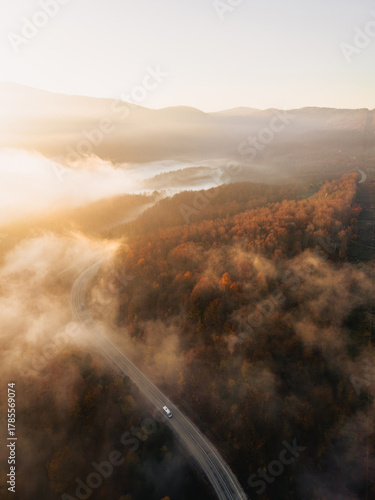 Aerial view of a single car driving on a winding foggy mountain road at sunrise