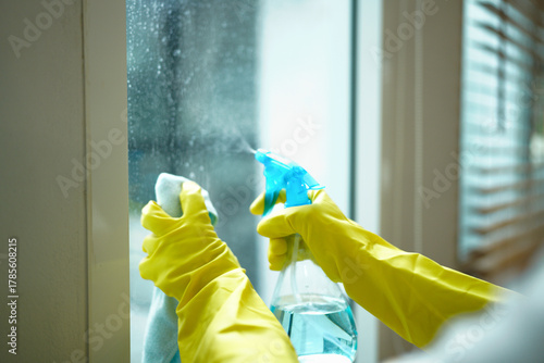 Konstfotografi Person wearing yellow gloves cleaning a window with a spray bottle and cloth