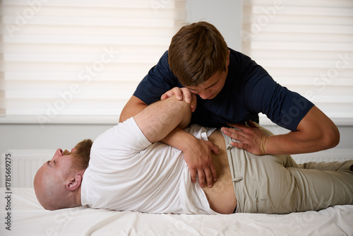 Chiropractor performing spinal adjustment on male patient lying on treatment table. Physiotherapist applying manual therapy for lower back pain relief, spine alignment, and rehabilitation in clinic.