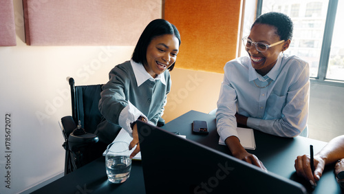 Two young women joyfully working together at an office table