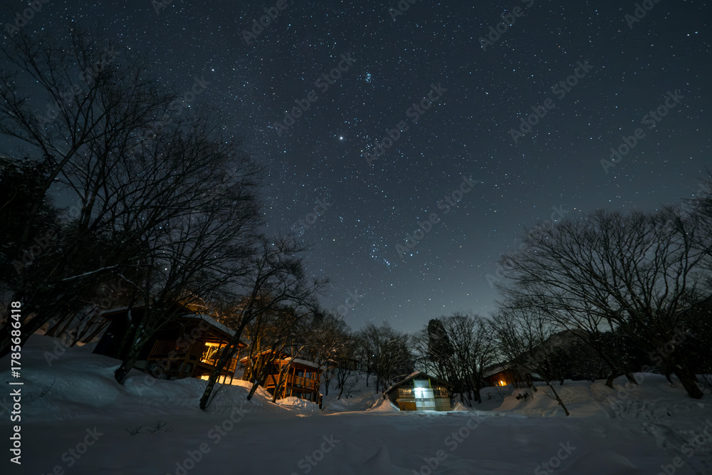 Fototapeta premium 冬の夜、雪原に輝く星と温かい光のキャビン