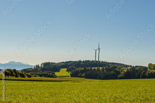 Two wind turbines stand on a hill with athe alps in  the background.