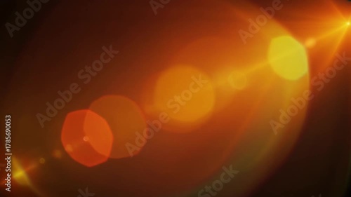 A vibrant optical lens flare with warm orange light leaks and glowing bokeh on a dark background.