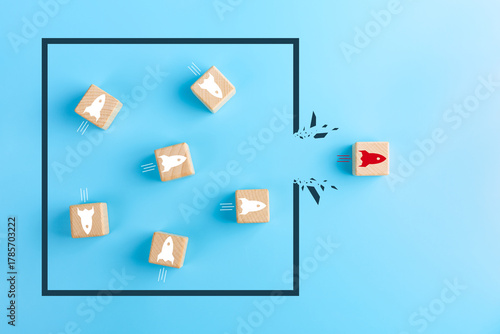 Concept of overcoming barriers, goal, target. Red wooden cube with rocket launch icon breaking through obstacle on blue background