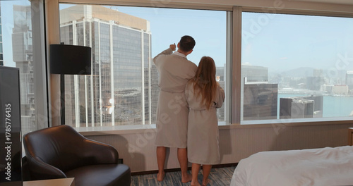 Behang Couple in hotel room wearing robes, admiring city skyline through large window, enjoying urban view, relaxation, travel