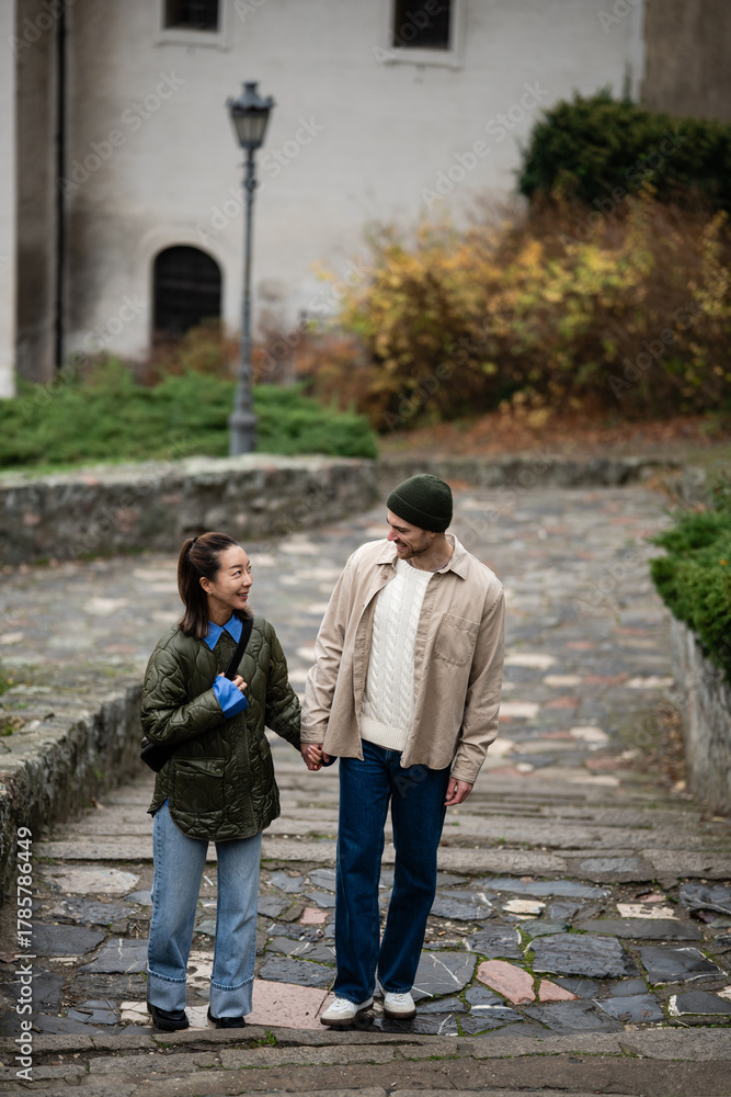 Obraz premium Happy multiracial couple walking hand in hand on city stairs